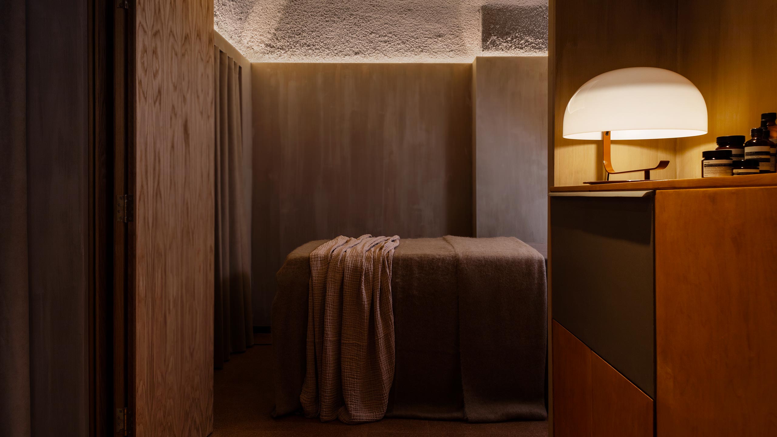 A dim-lit facial treatment space; a bed sitting in the centre of a room.