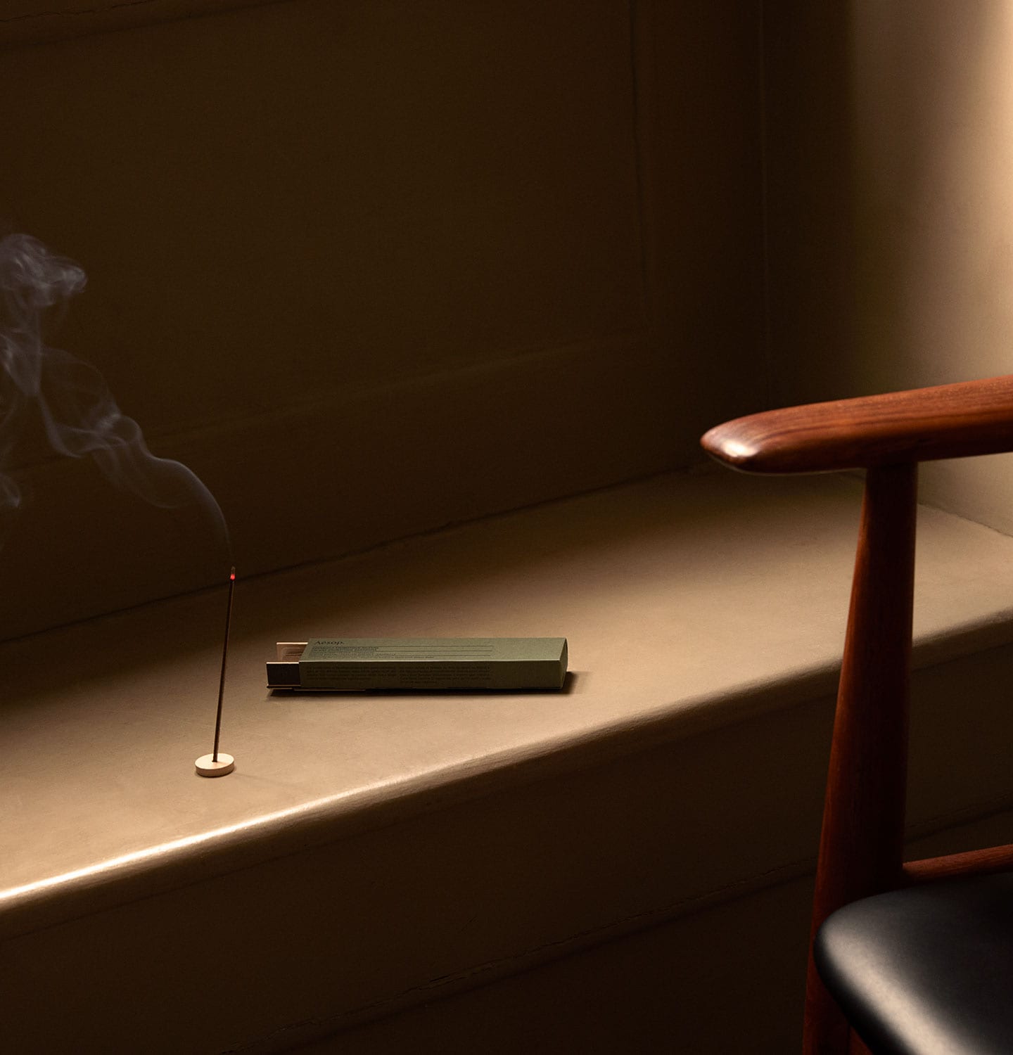 Aesop aromatique incense burning on a brown ledge next to a chair