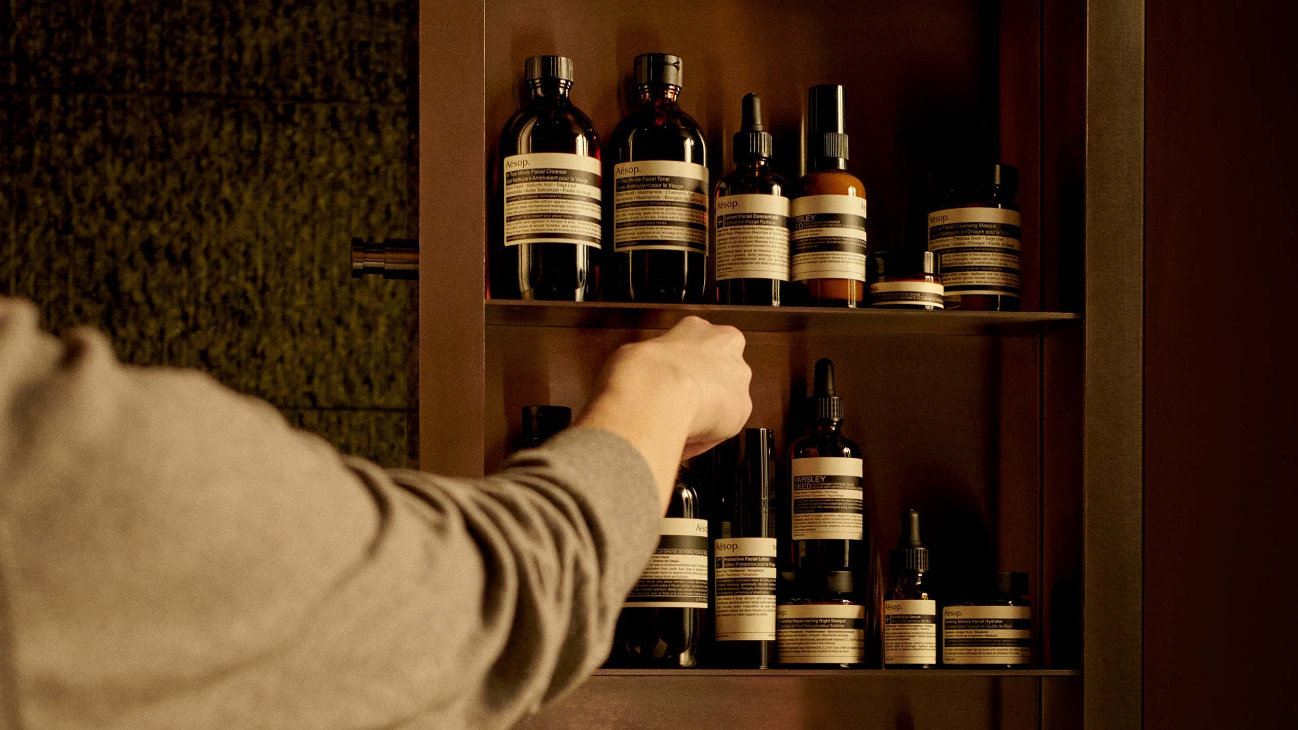 An Aesop store consultant hand selecting a product from shelving.