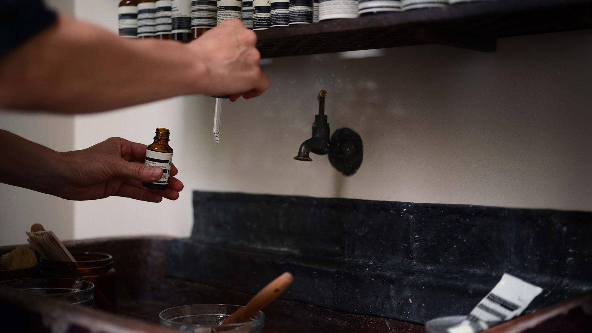 An Aesop consultant holding a small amber bottle along with a pipette over a basin.