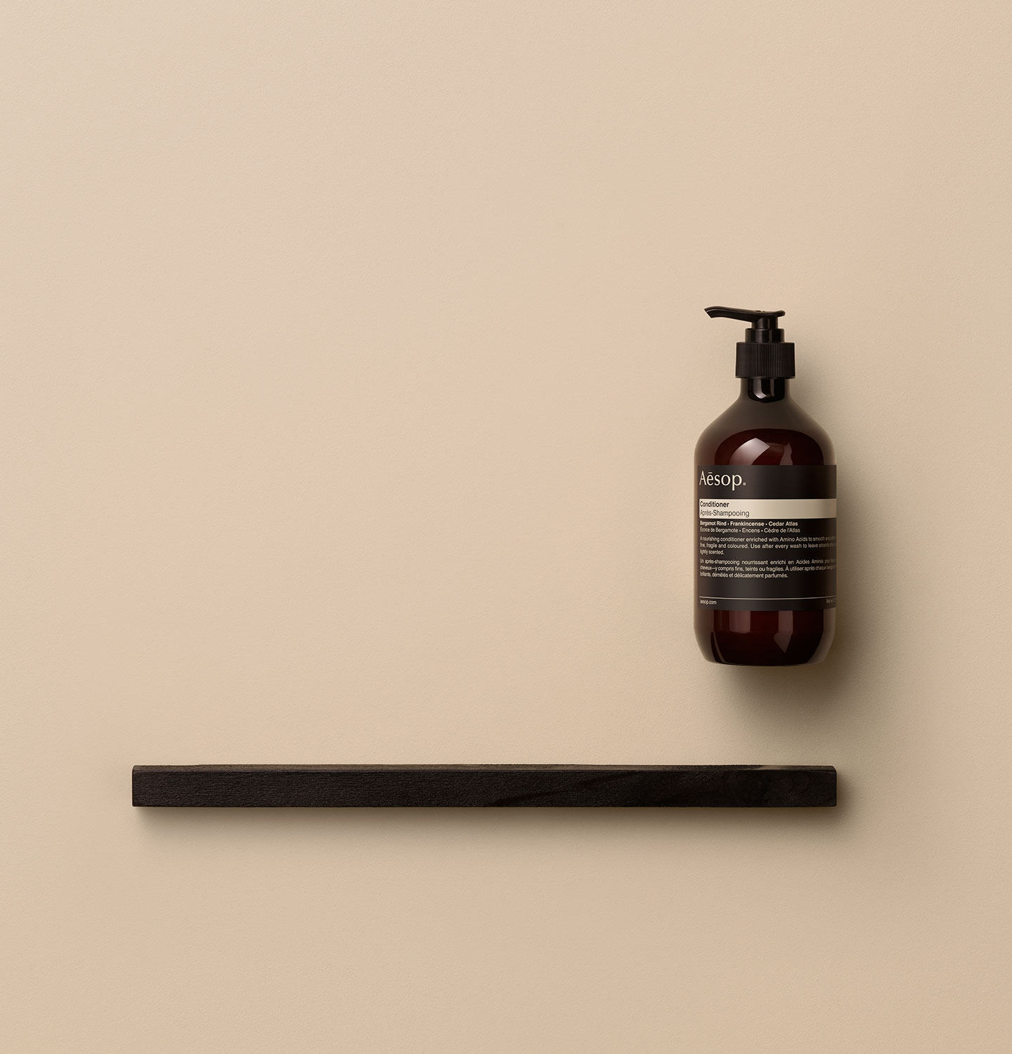 Amber pump bottle arranged alongside a dark wooden object on a pink textured surface.