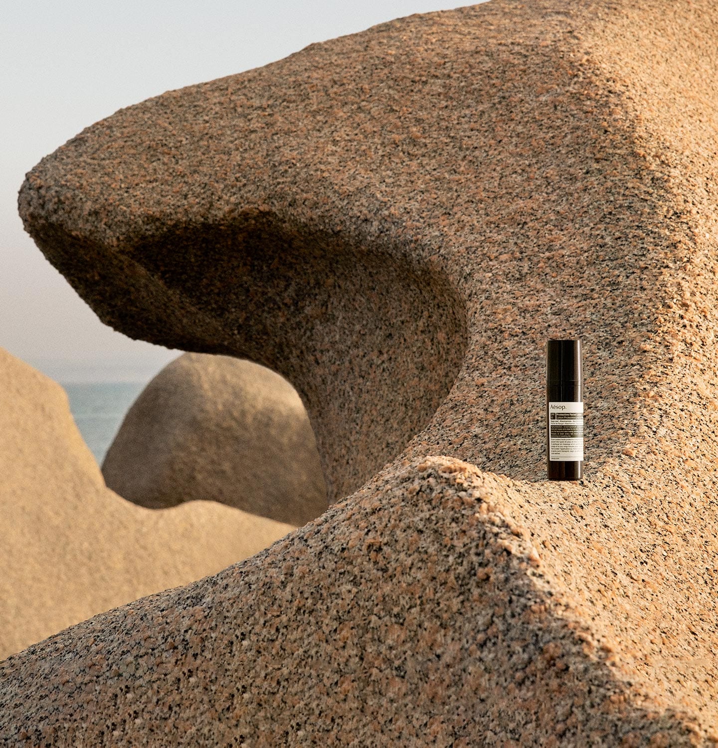 A bottle of Protective Facial Lotion SPF50 resting on a rocky shoreline.