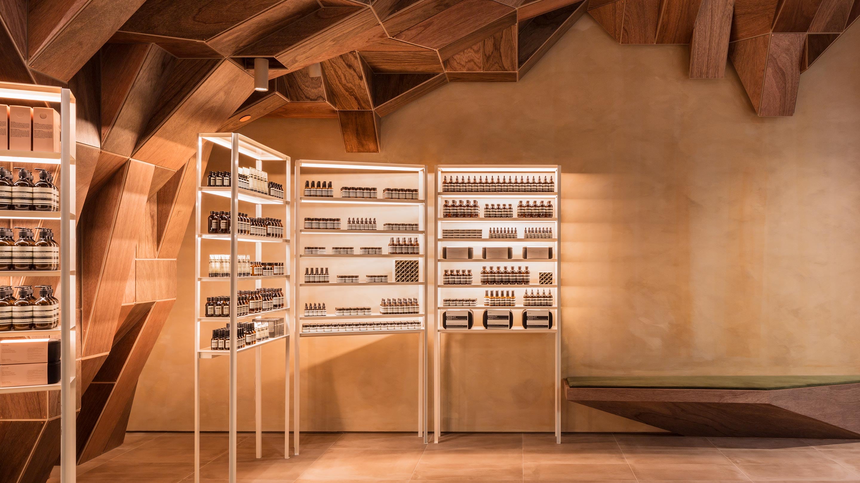 Powder-coated metal walls with shelving units that feature built-in lighting. The ceiling is crafted by dark plywood in a sporadic, angular pattern.