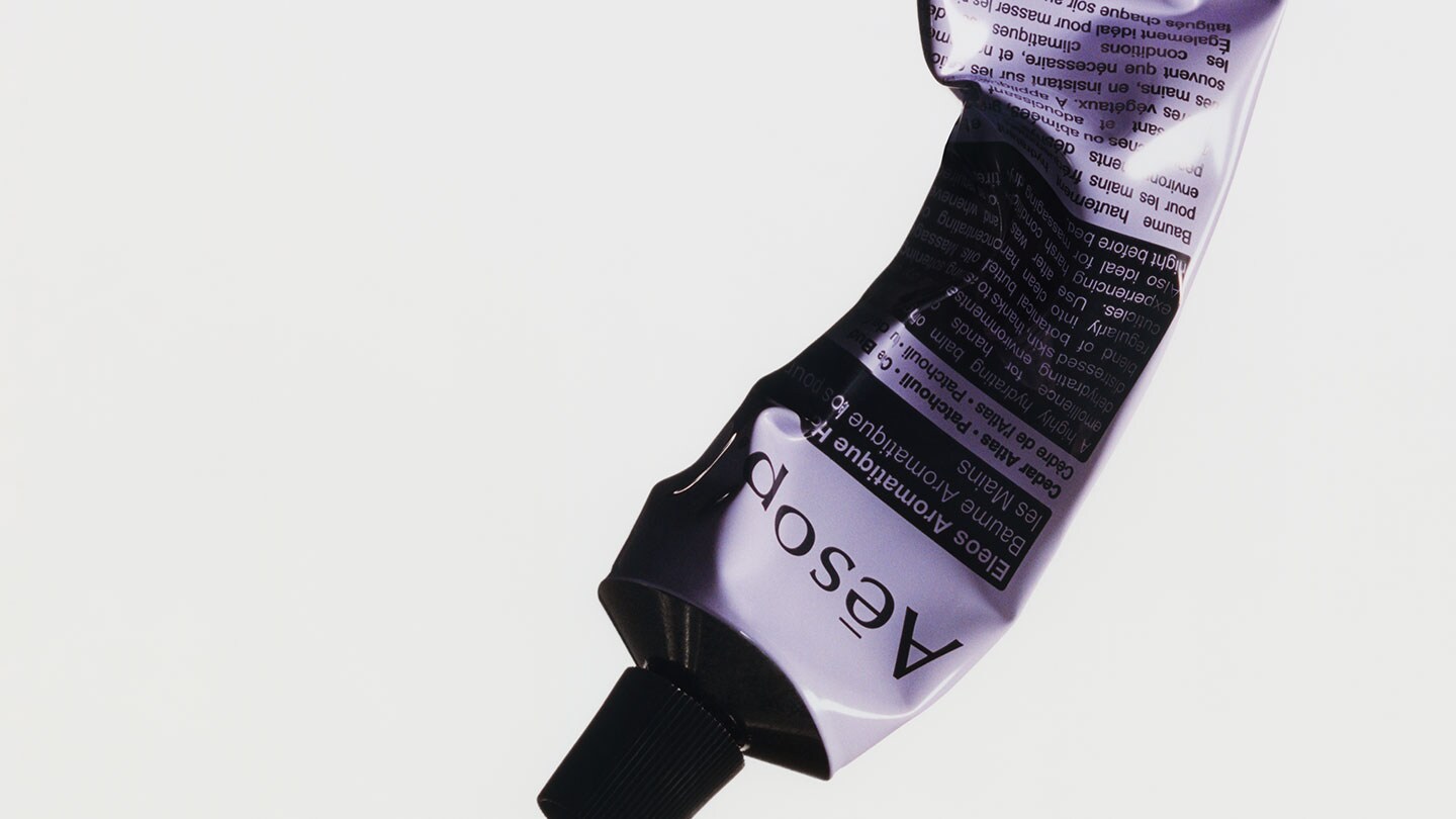 Squeezed Elos hand balm tube in grey background