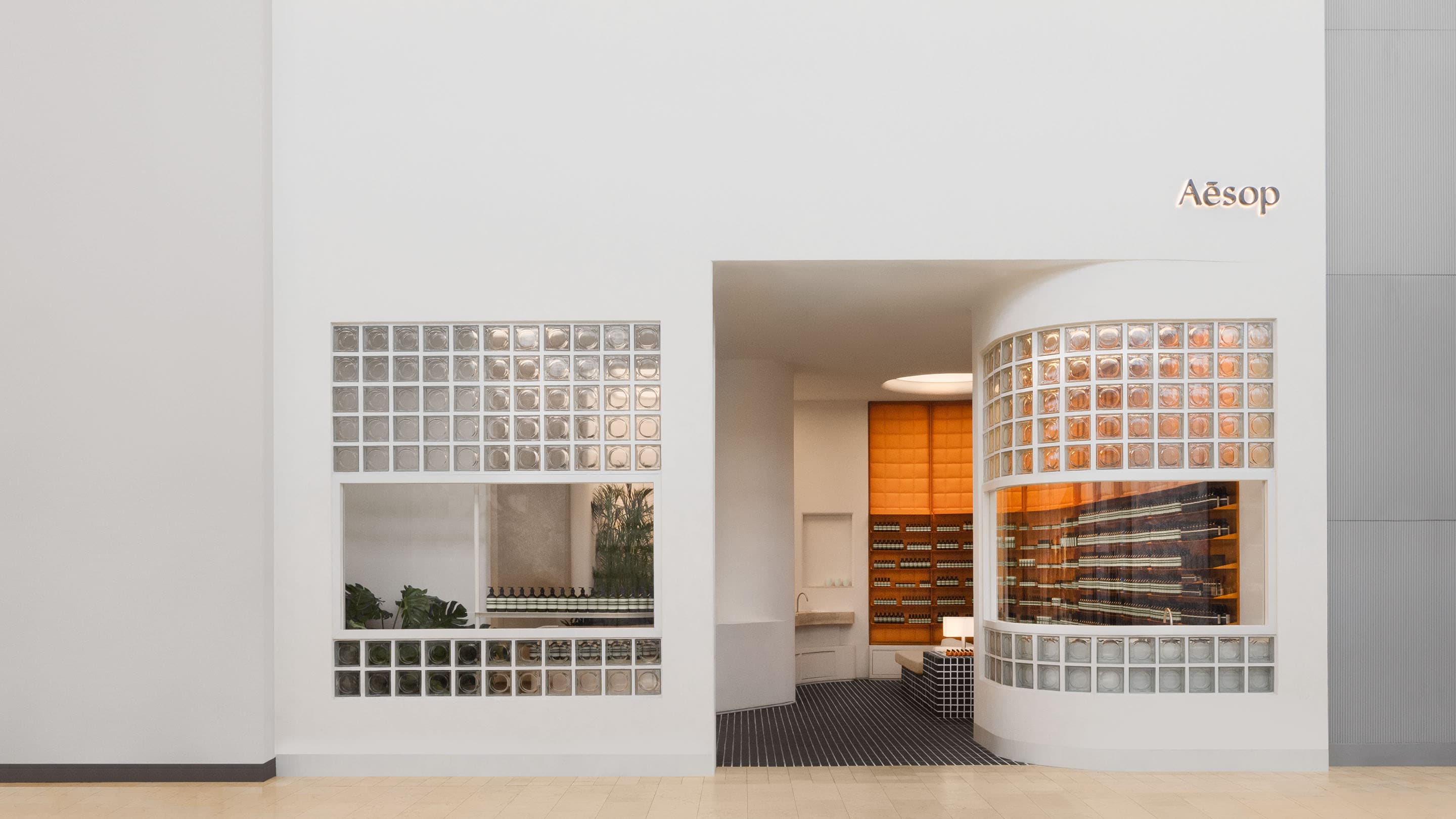 aesop square one storefront with white facsade featuring glass blocks, with orange drawers visible in back of store