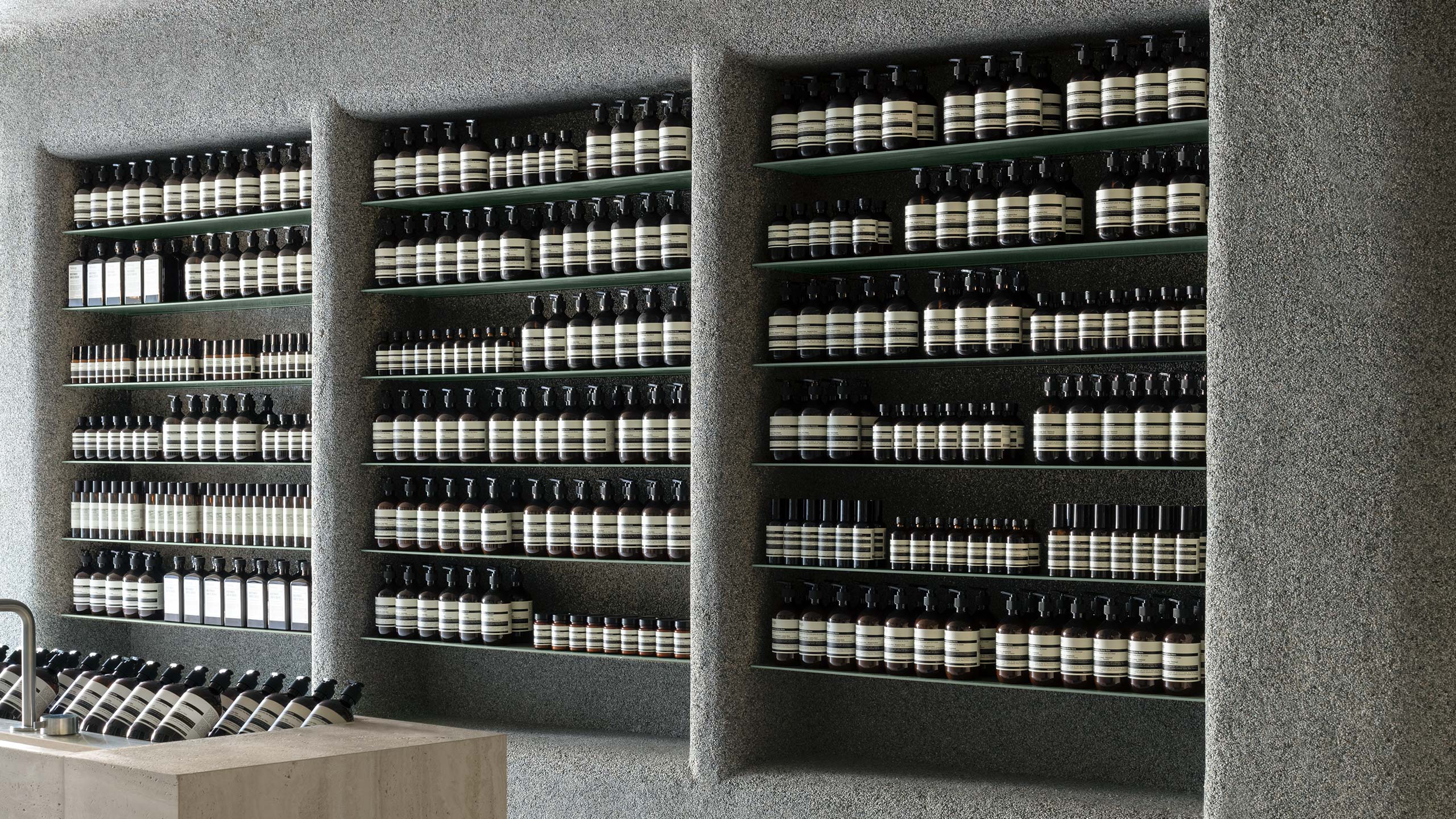 Textured concrete shelving displaying several black Aesop bottles.
