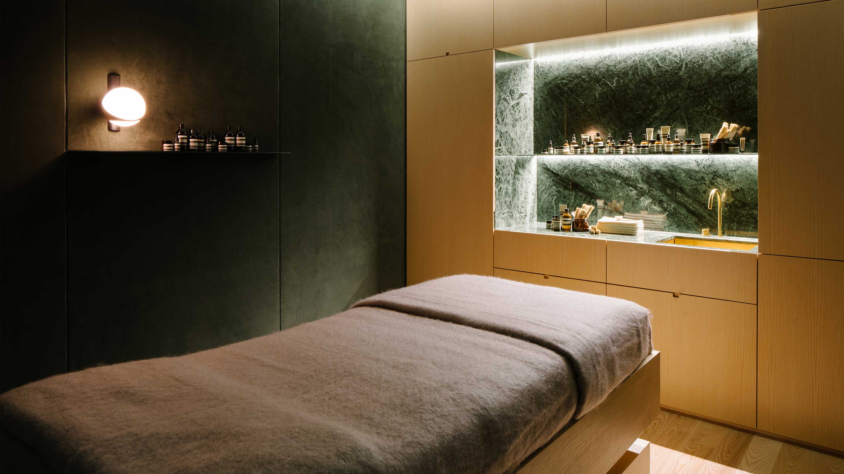 The interior of the facial room, with a bed for customers. The room features a dark green feature wall and a basin for the customer service assistant. 