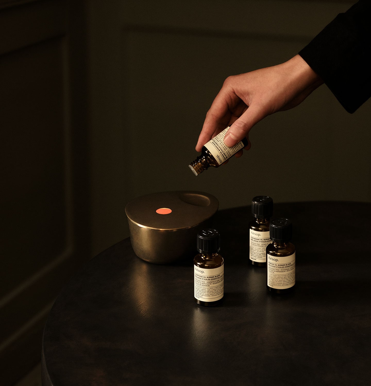 Hand adding Aesop oil burner blend into the bronze oil burner