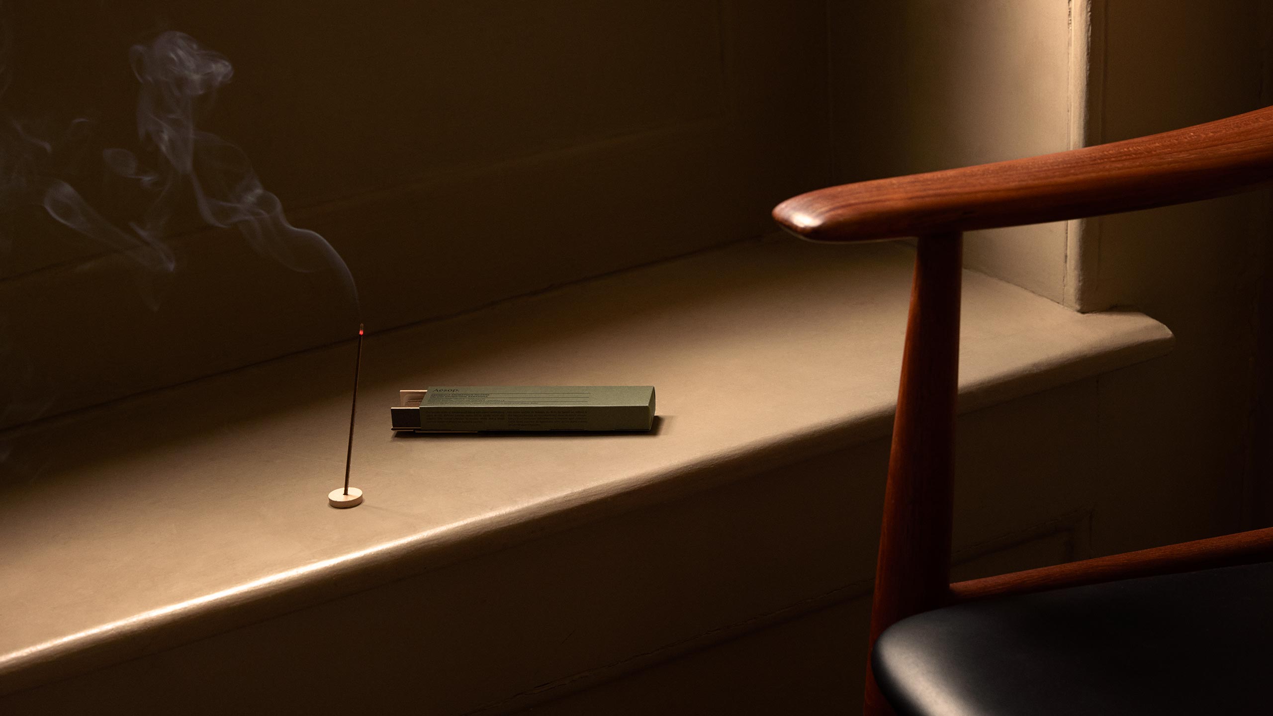 A lit stick of incense sitting alongside a mid-century chair.