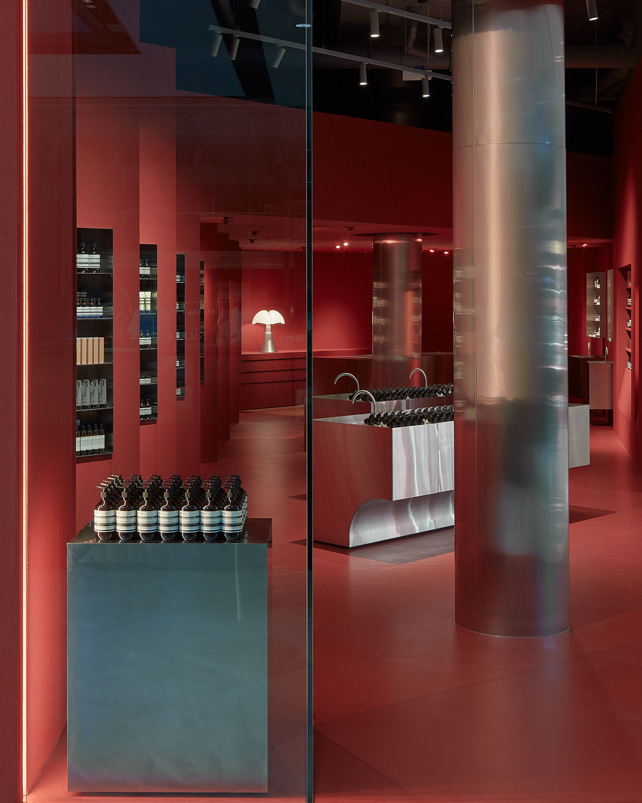 A brushed stainless steel counter stocks Aesop products. There is a tall pillar in the centre of the store.