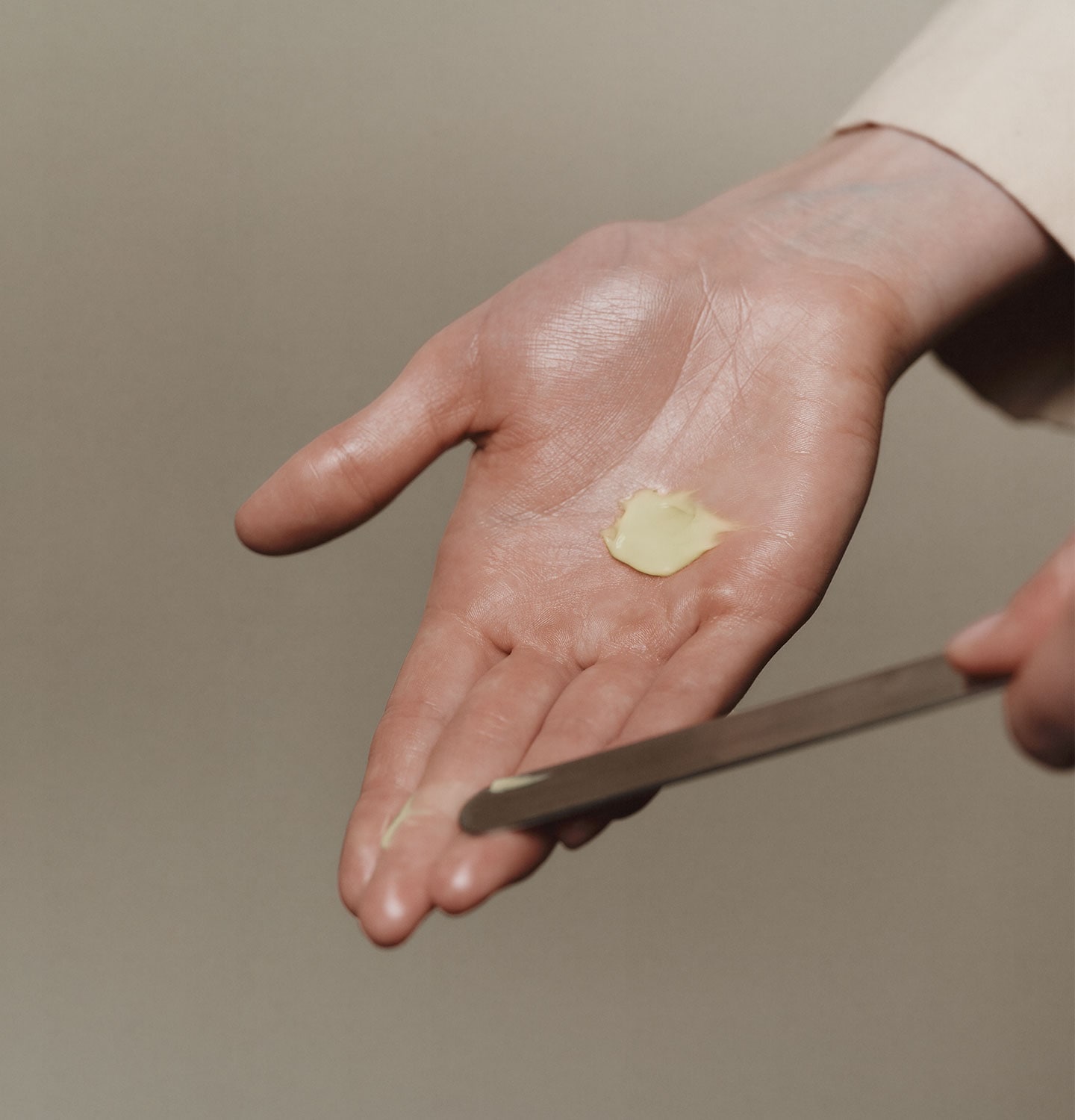 A metal spatula and a cream product touching a palm of a hand