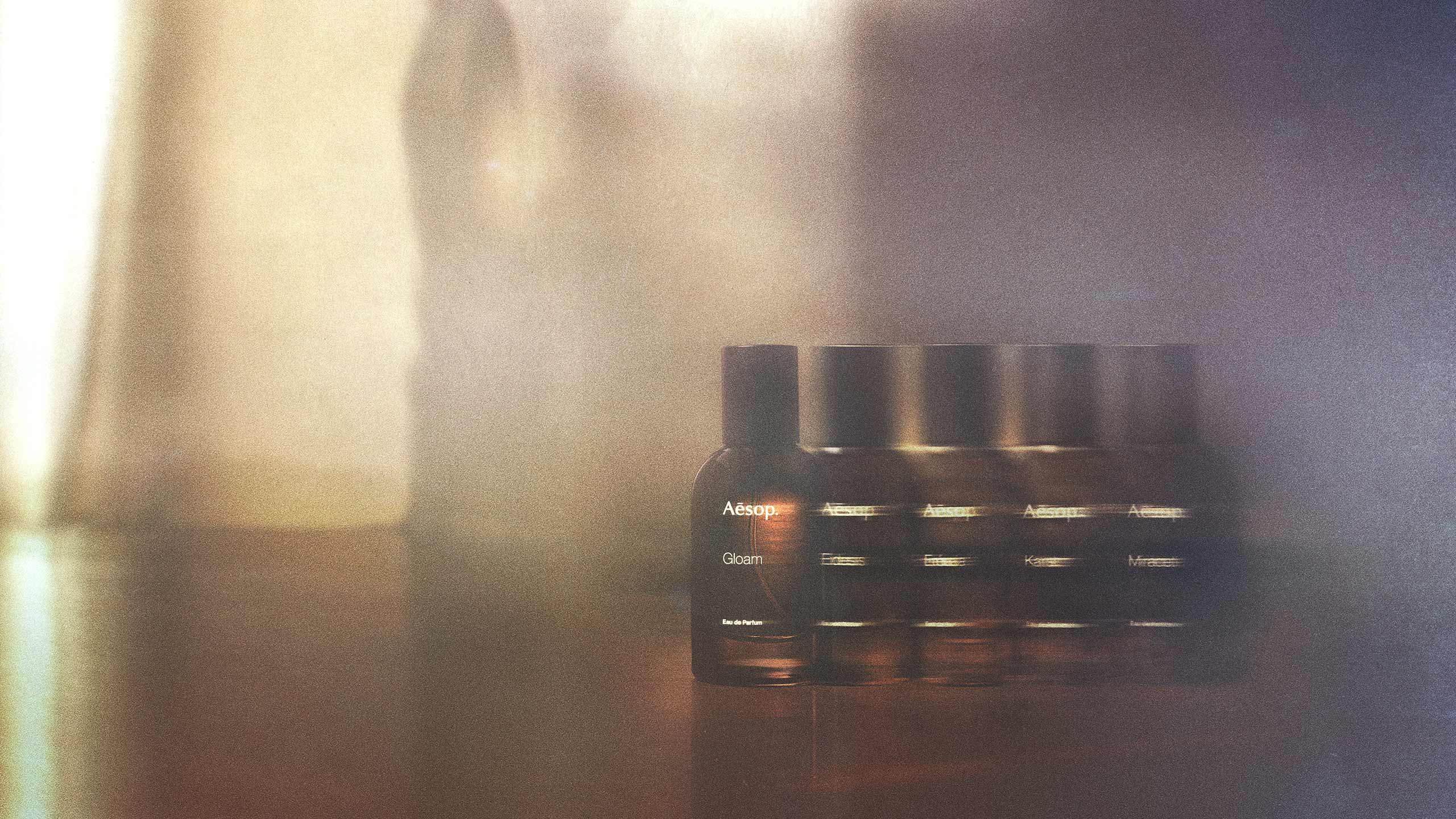 Gloam EDP in amber spray bottles on wooden surface in blurred textured background