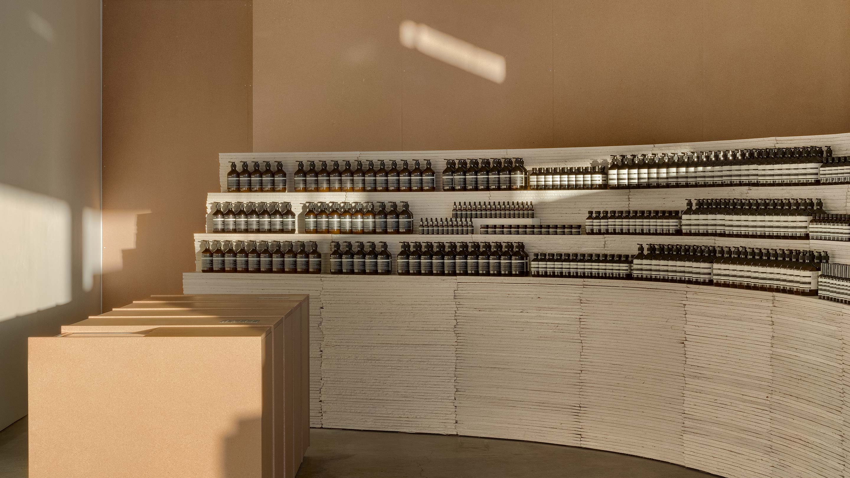 Fragmented light passes shines onto soft-beige coloured walls; Aesop product sit neatly around a curved stack of drywall panels.