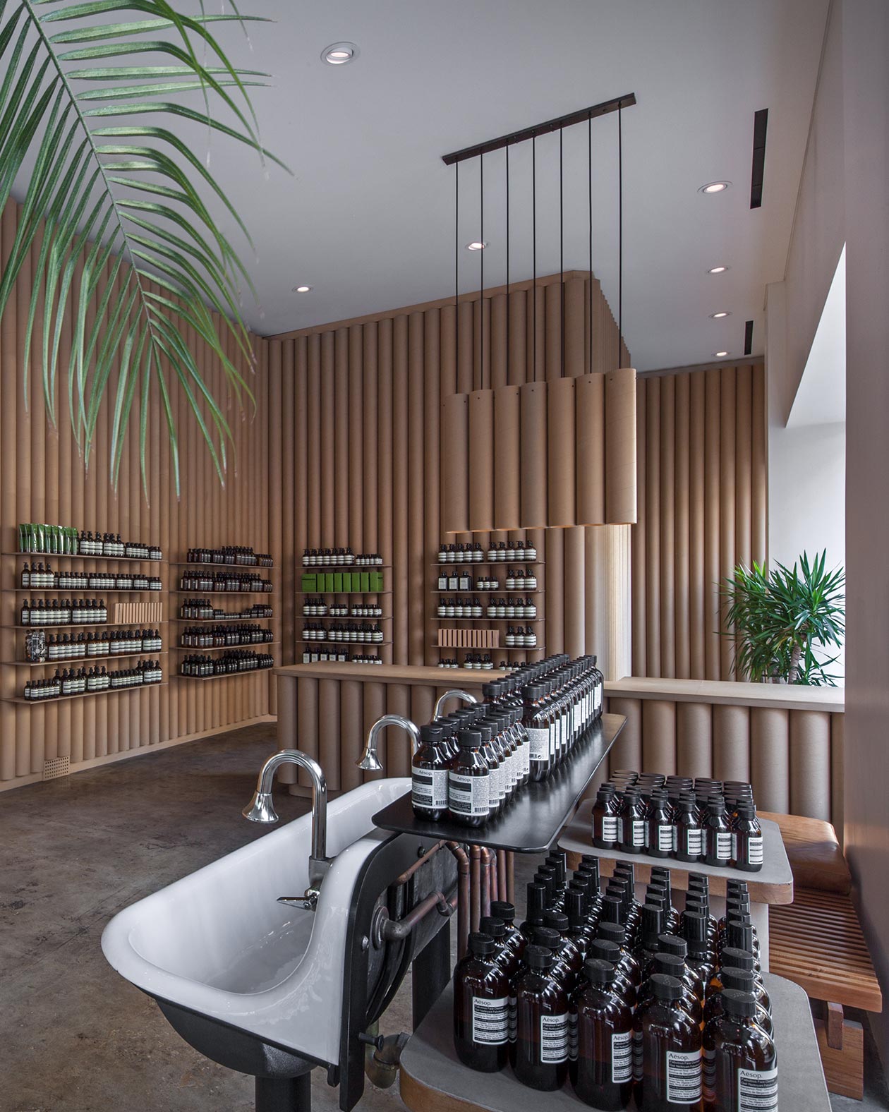 A white basin holding Aesop bottles in the foreground; a store counter fitted with cylinder cardboard tubes in the background.