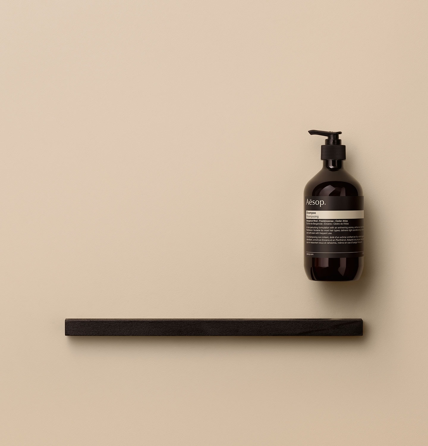 Amber pump bottle arranged alongside a dark wooden object on a pink textured surface.