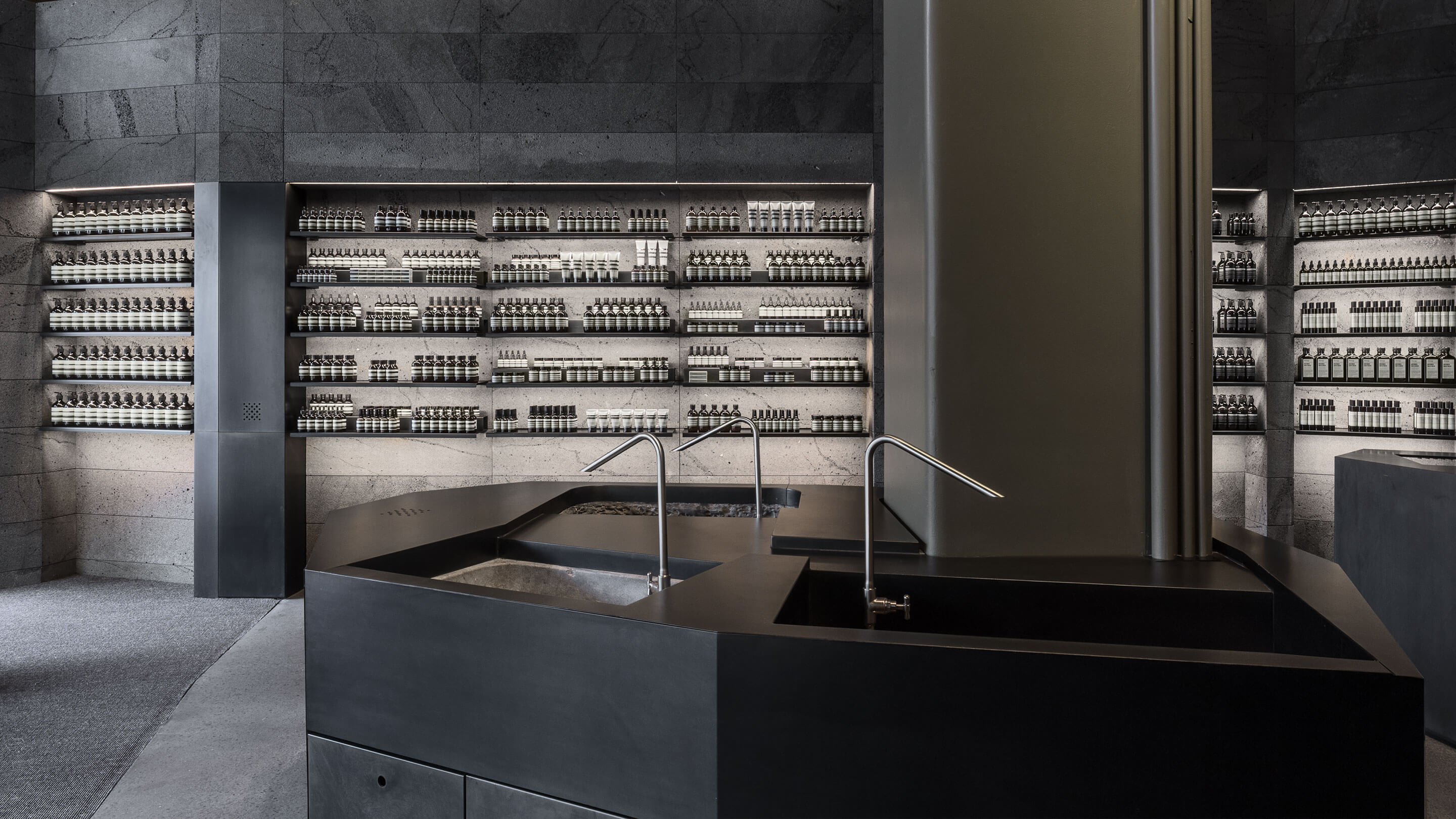 Dark stone interior of the store, with a black customer service basin with dark steel fixtures.