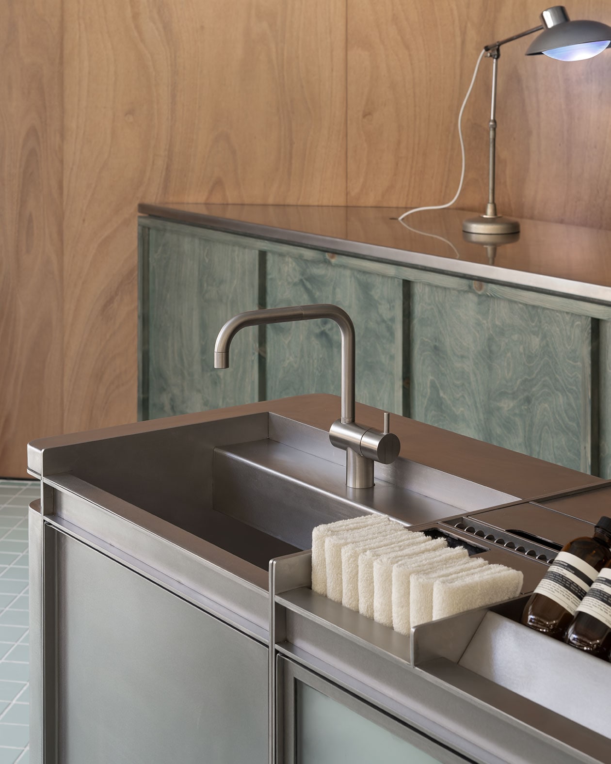 Aesop products and white hand towels placed next to a metal sink in Aesop Booragoon store