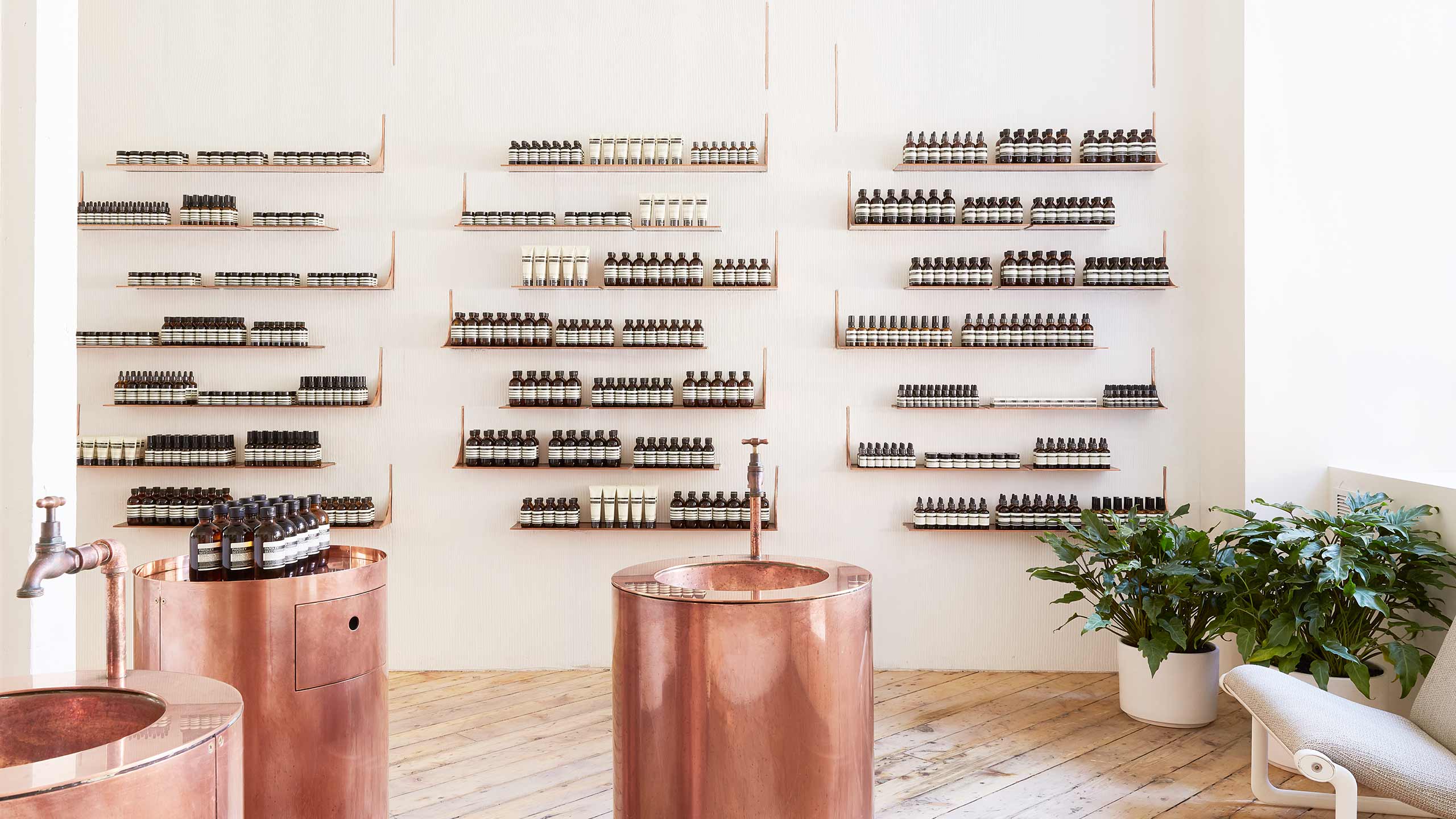 Brass sinks sit in the centre of the store with white shelves holding Aesop product.