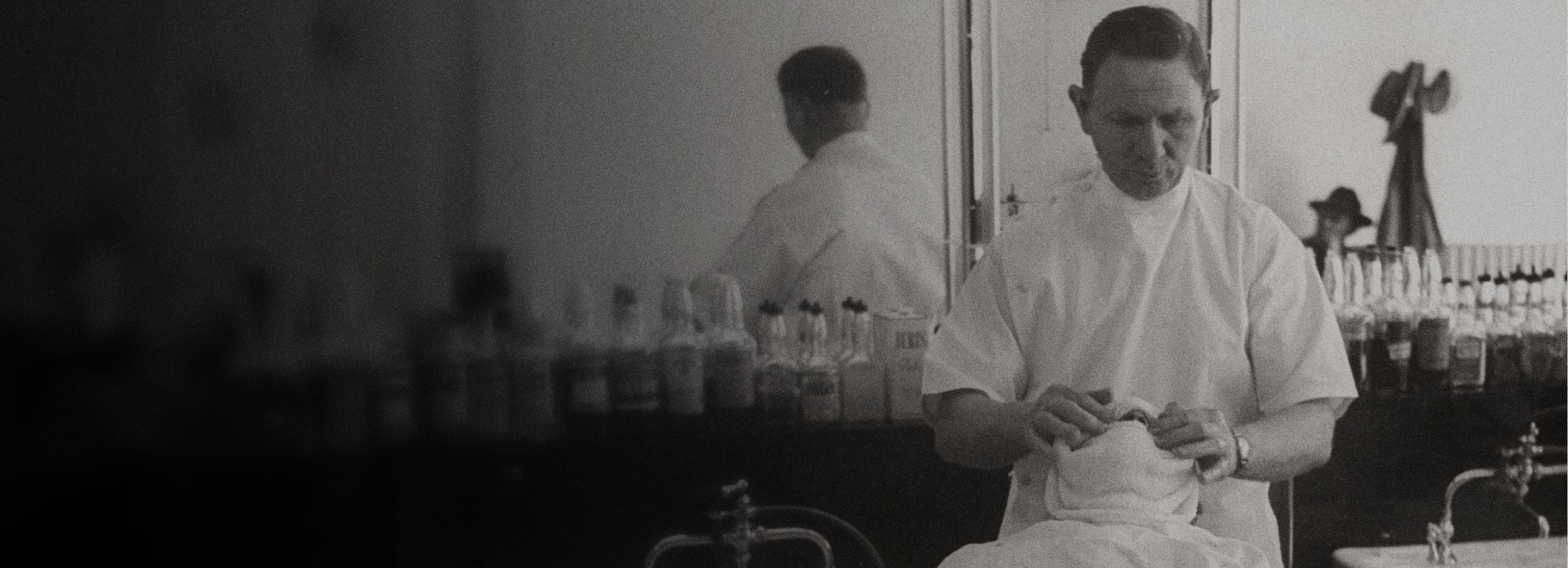 A black and white photo of a barber preparing for the grooming process with a customer at a salon
