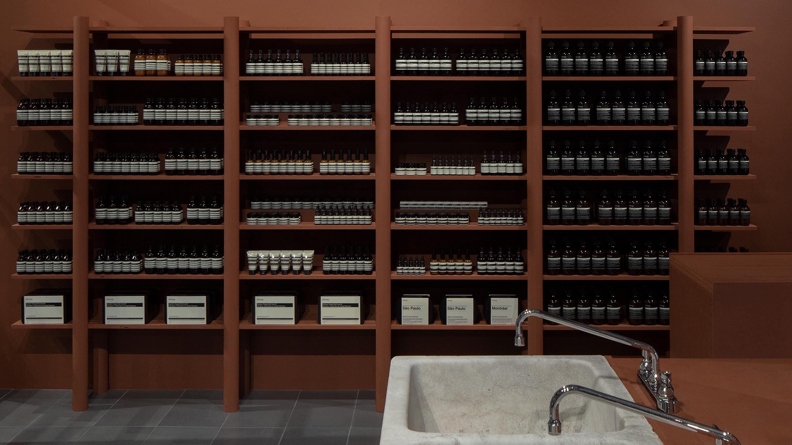 A profile view of sienna coloured shelving holding Aesop product.