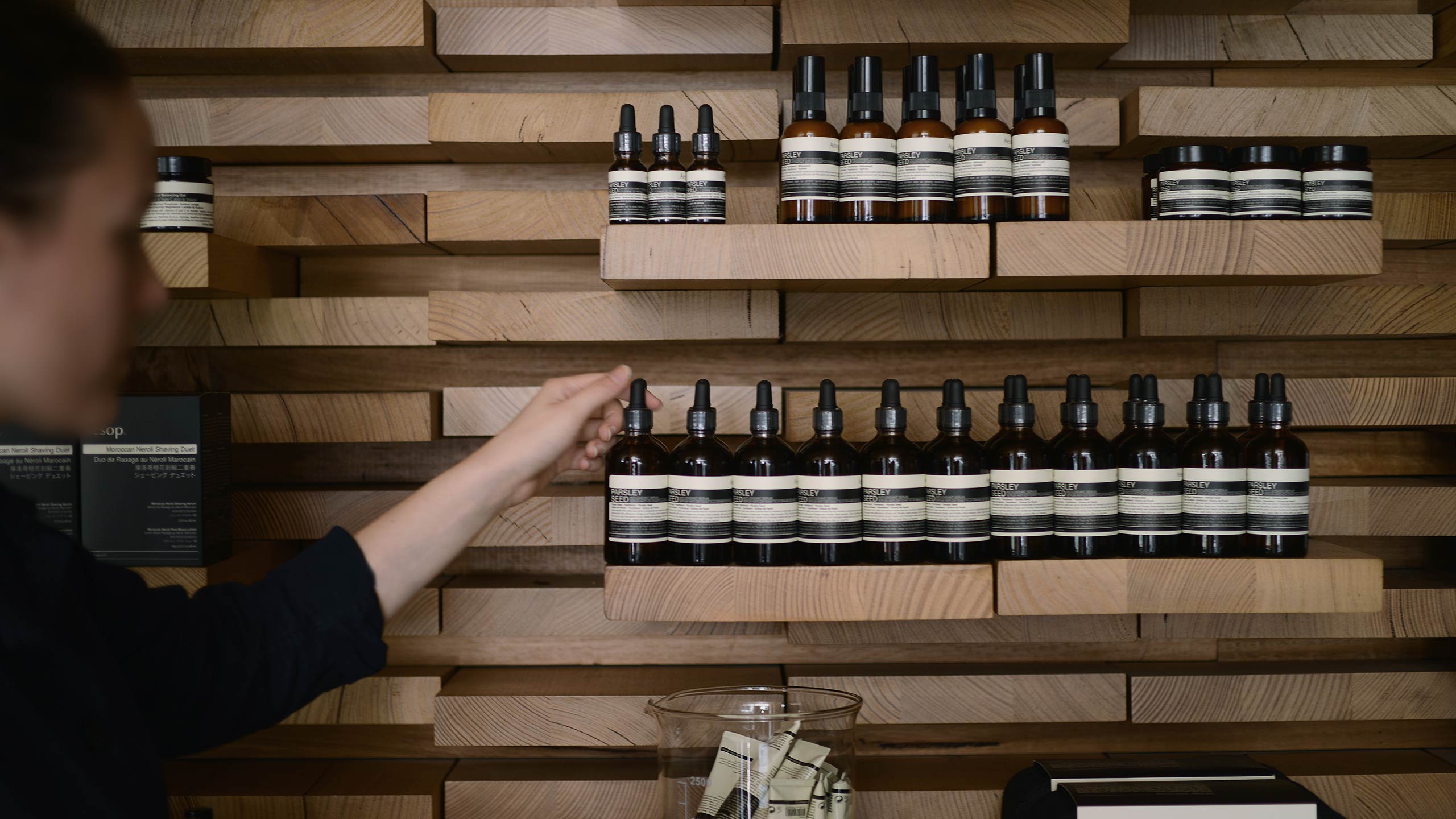 Image of an Aesop employee reaching for a shelf of Aesop product