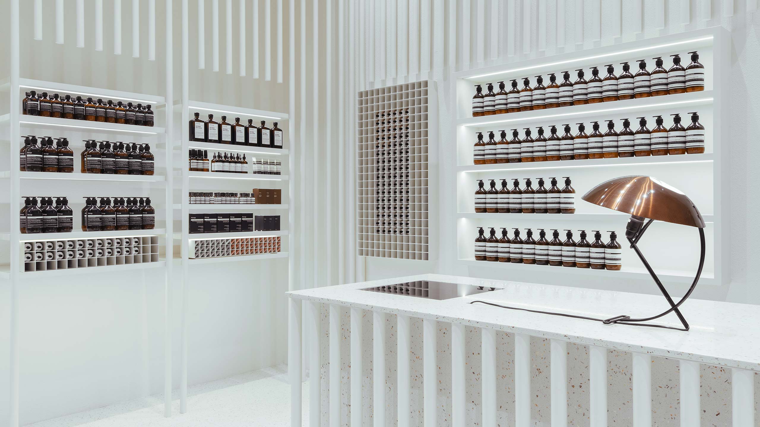 Bright white interior showcasing an array of Aesop products on white metal shelves. 