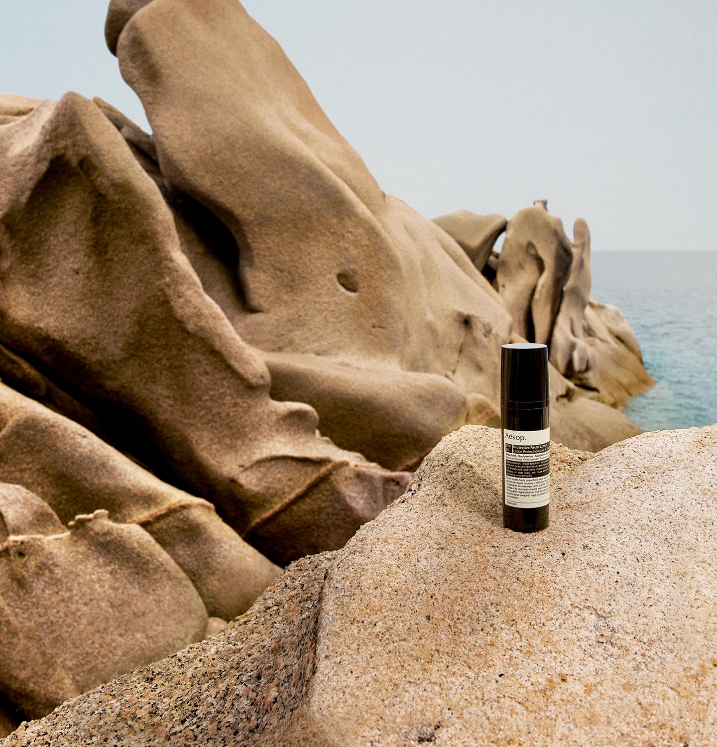 A bottle of Protective Facial Lotion SPF50 resting on a rocky shoreline.