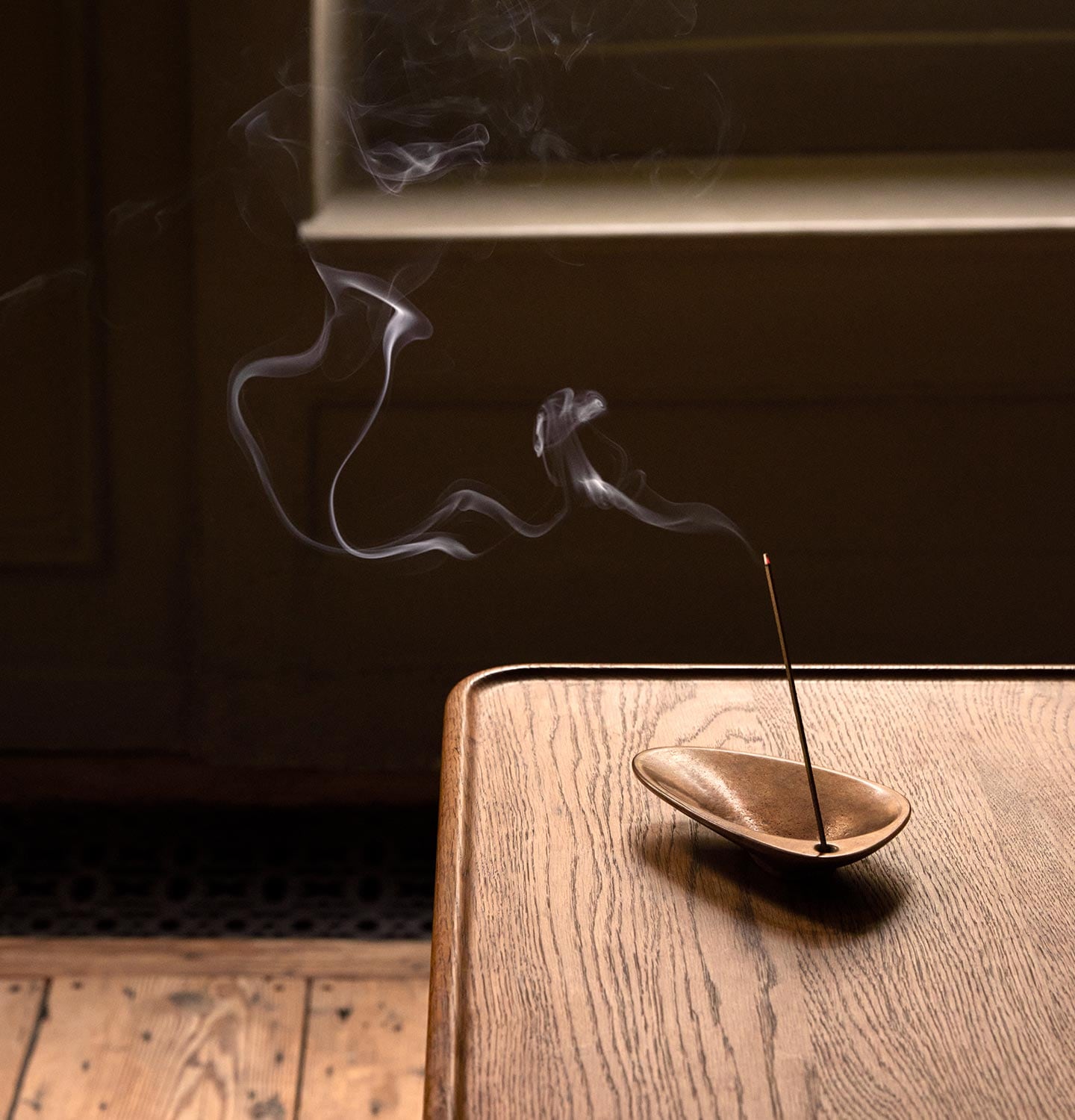 Aesop bronze incense holder with burning incense on top of a wooden table