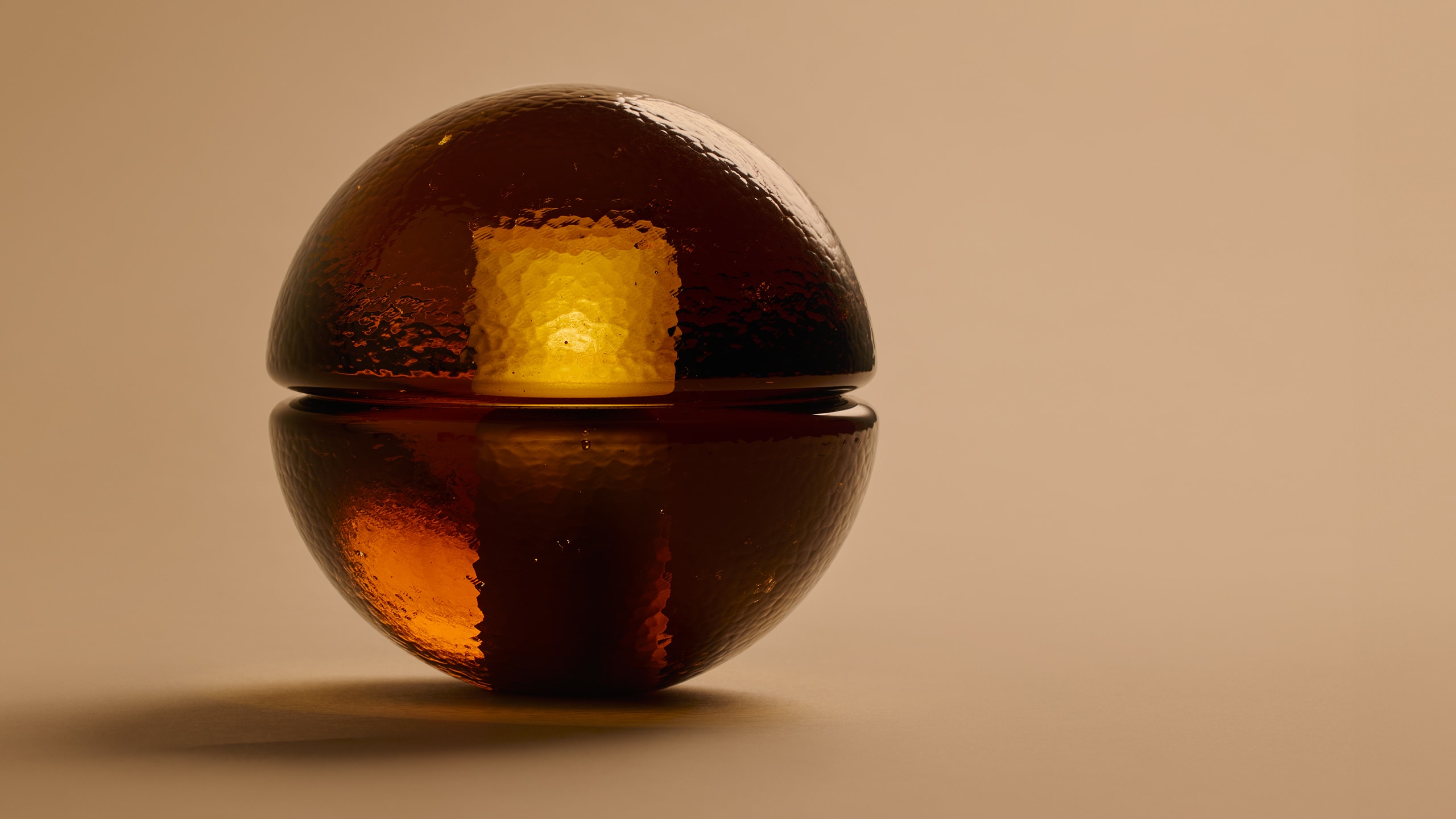 tight shot of Bocci 14p amber glass lamp illuminated and casting a shadow on a solid tan background