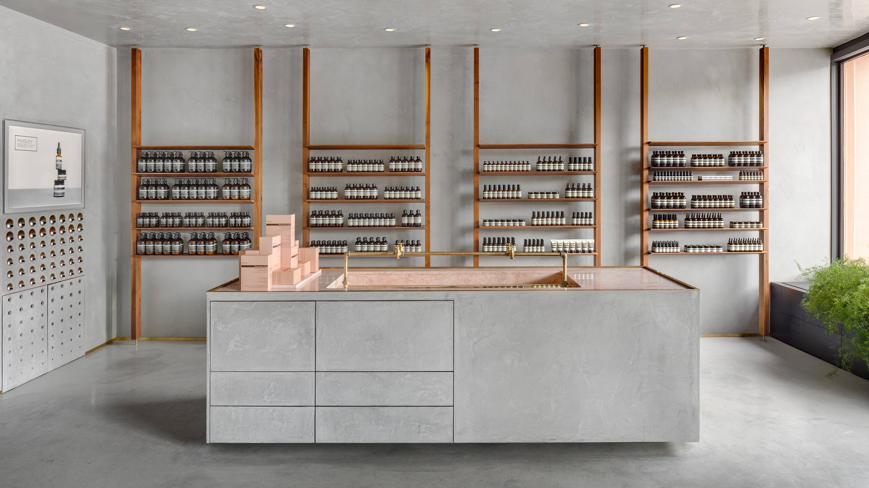 A wide matte-grey plastered sink with a marble pink basin sits in the middle of the frame surrounded by Aesop product.