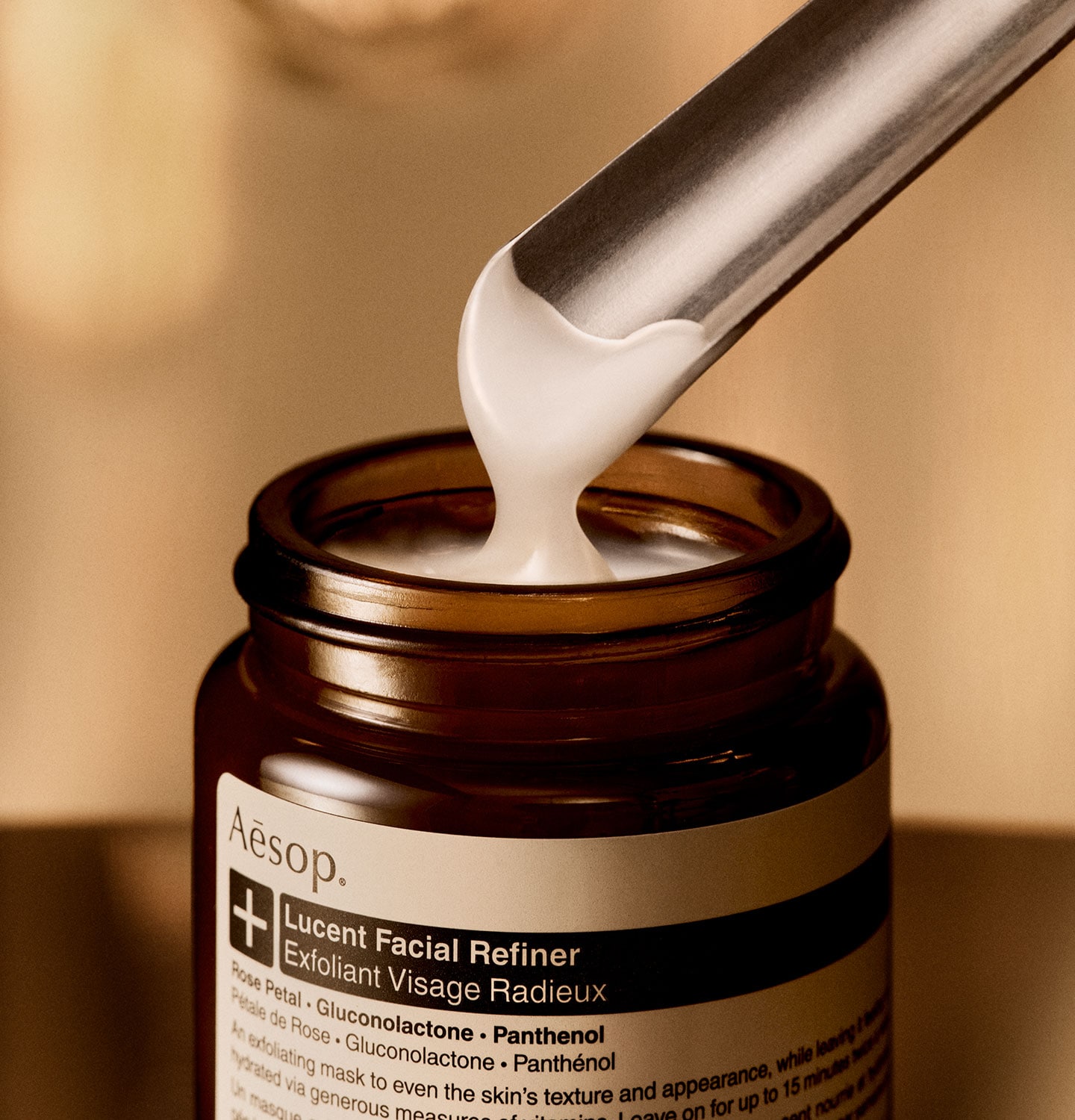 Aesop Lucent Facial Refiner texture with metal spatula and open bottle.